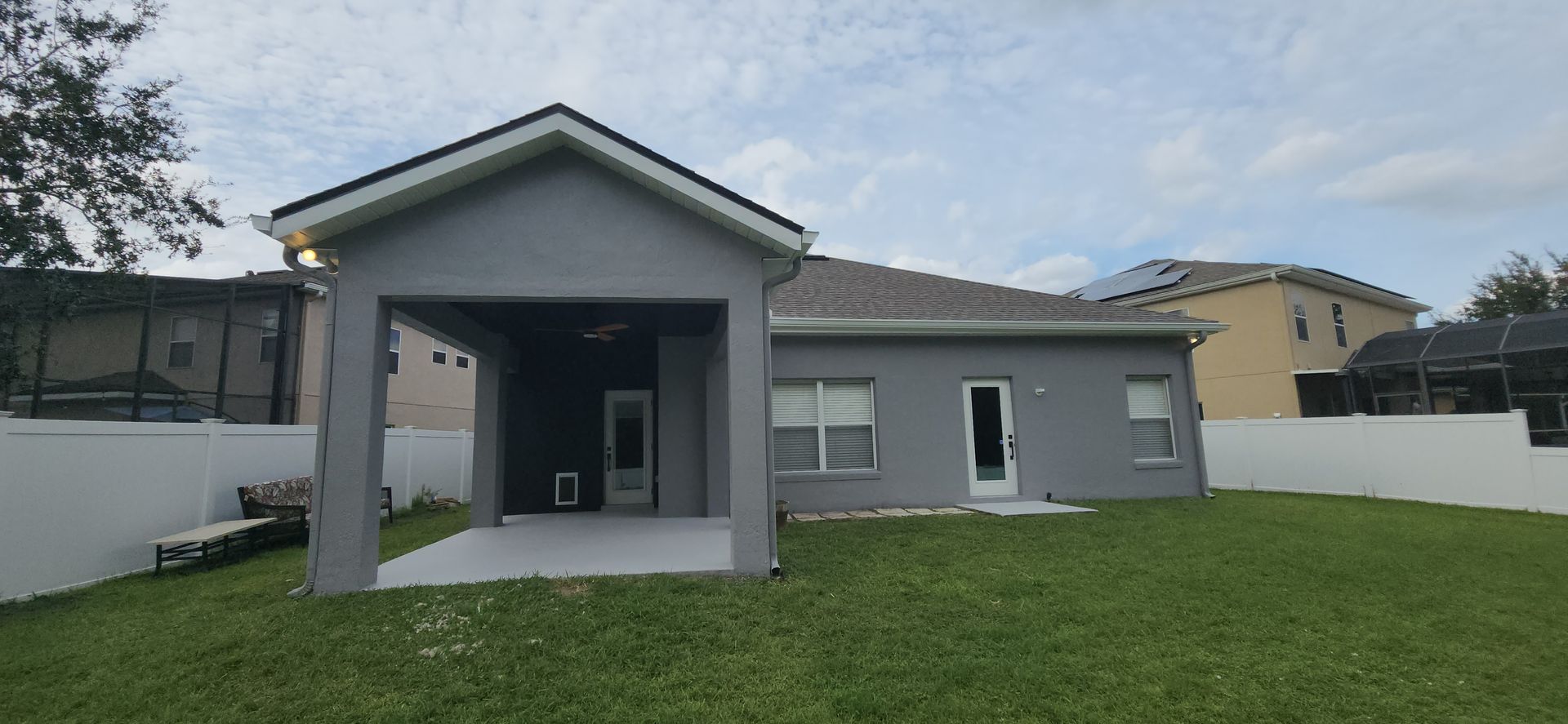 The back of a house with a covered porch and a white fence.