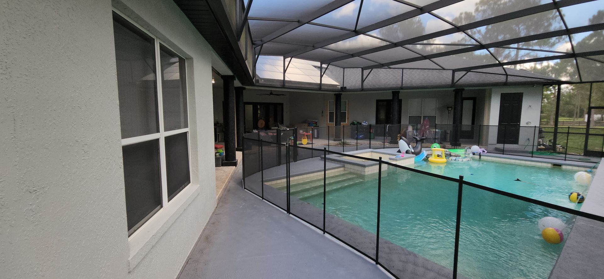 A large swimming pool is surrounded by a fence and a screened in area.