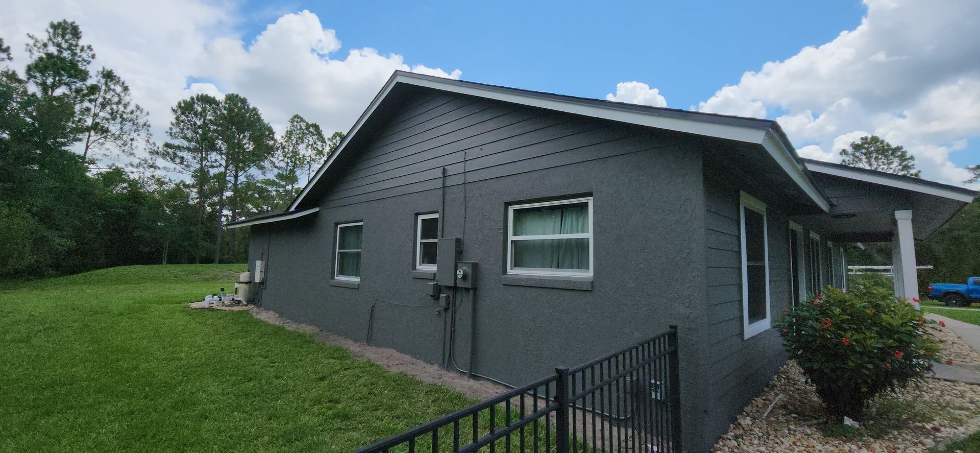 A gray house with a fence in front of it is sitting on top of a lush green field.