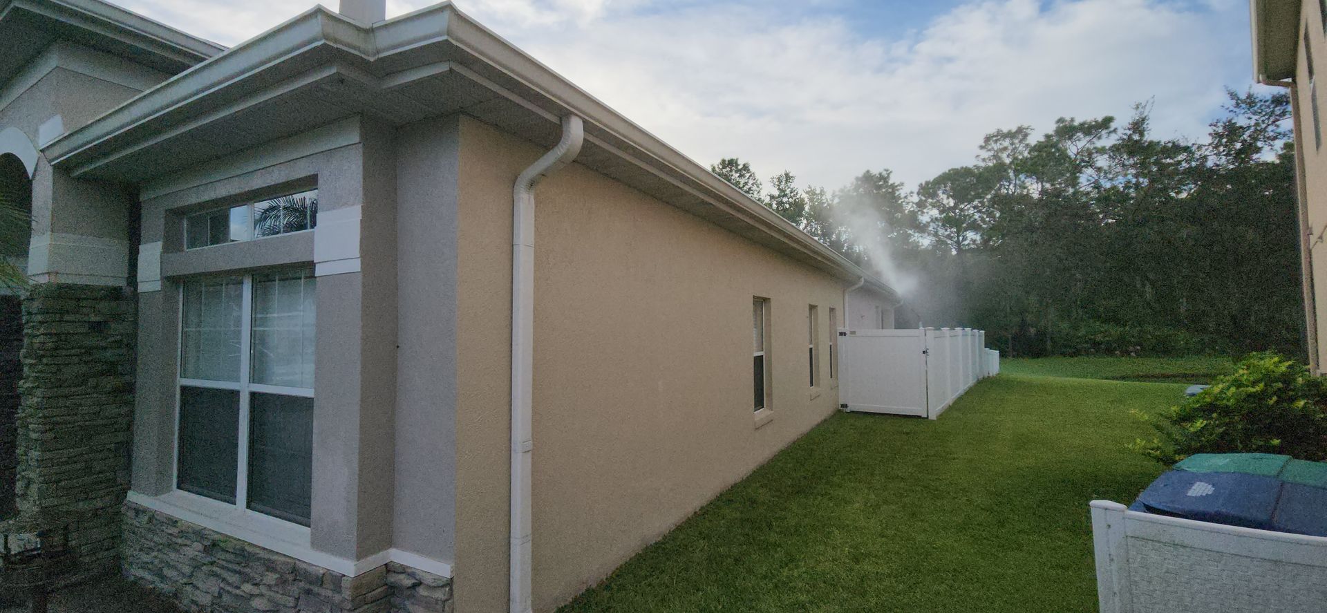 A house with a white fence in the backyard is being sprayed with water.