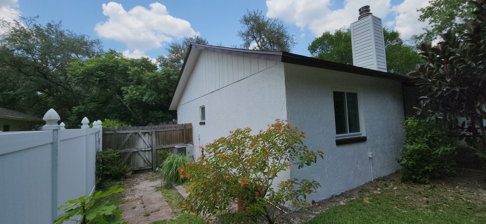 The back of a house with a covered porch and a white fence.