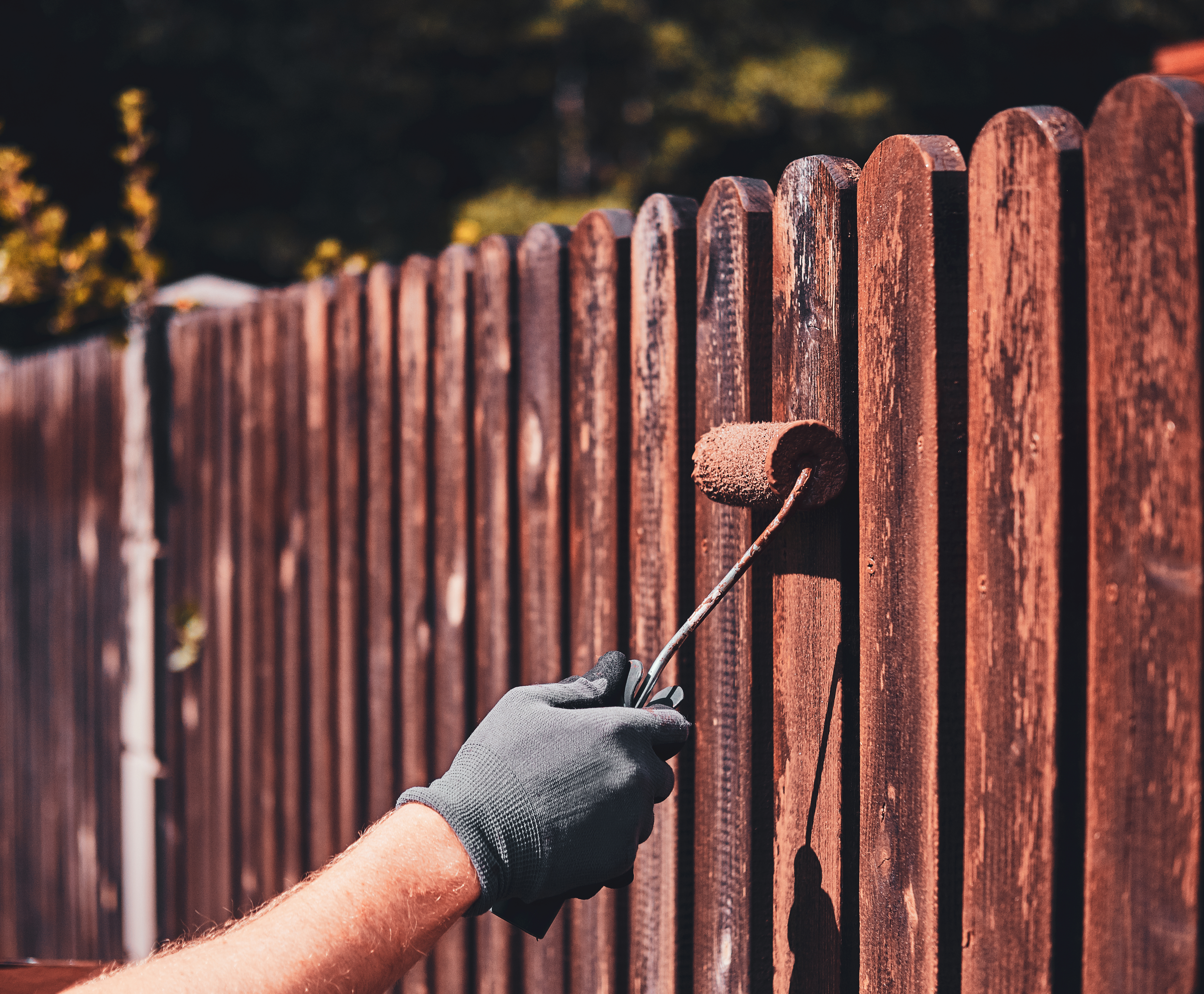 Painter in protective gloves painting a wooden fence on a bright summer day in Orlando.