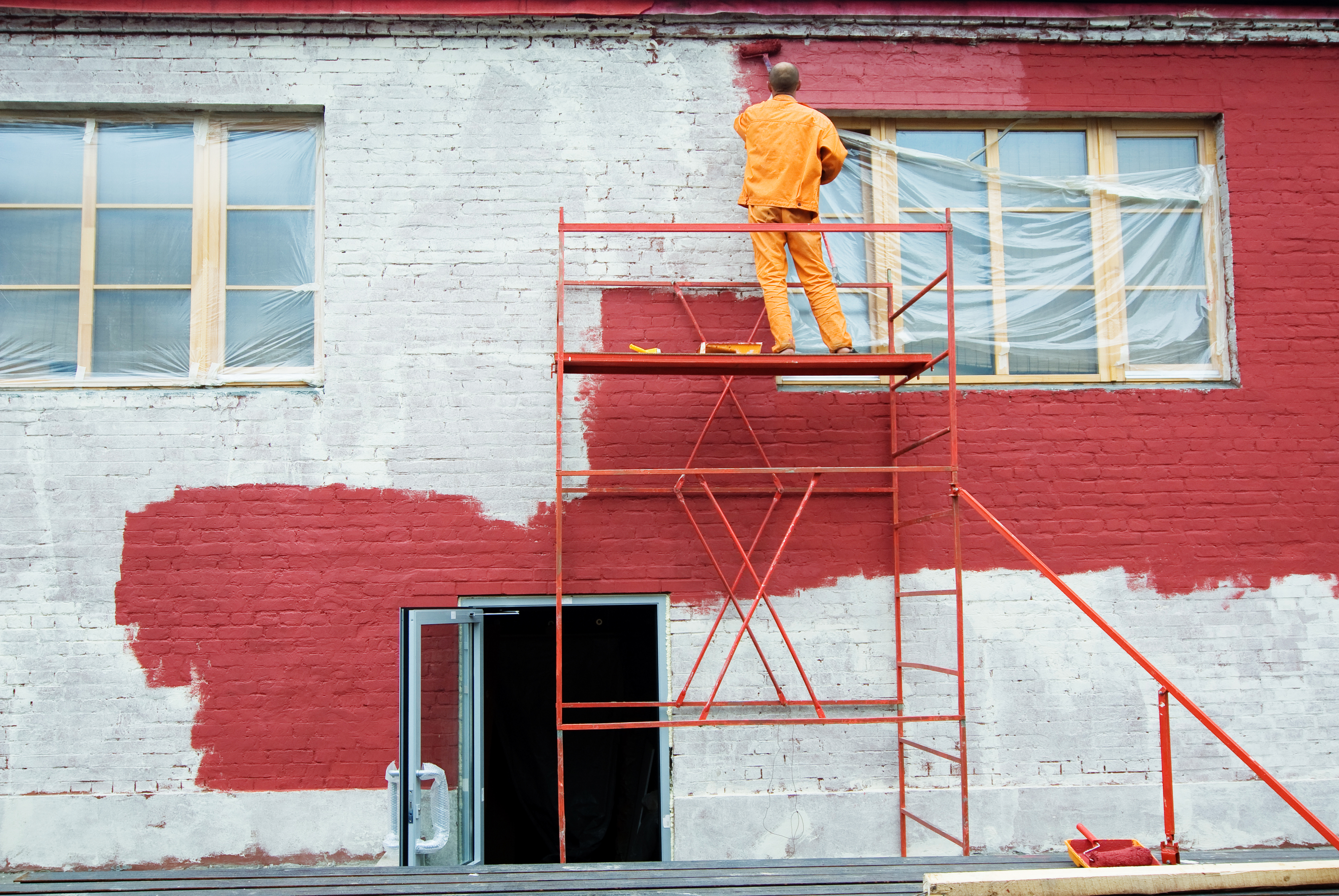 Close-up of a brush applying rich red exterior paint to a surface.