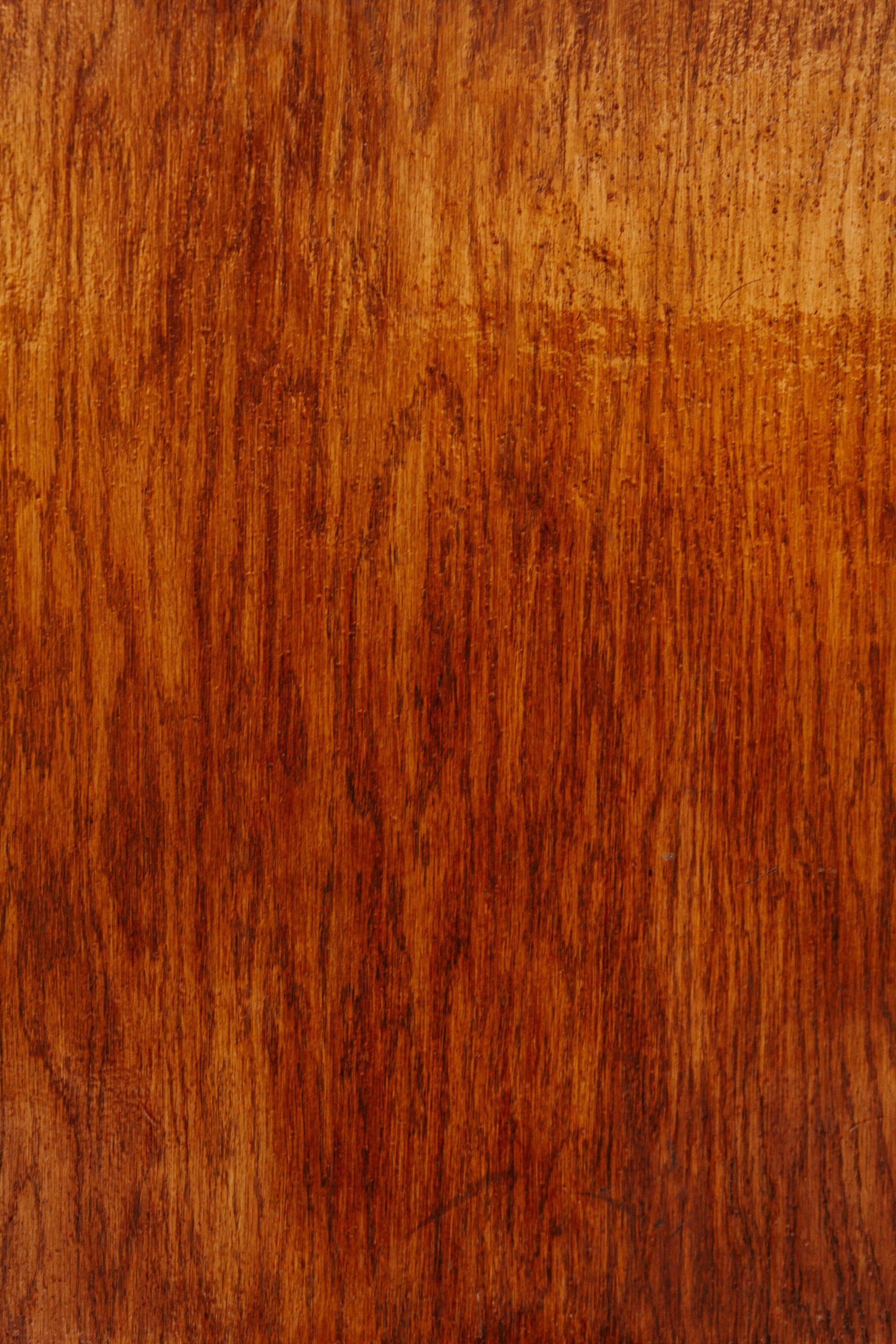 Close-up of a richly stained wood surface, showcasing prominent grain lines in shades of brown and red.