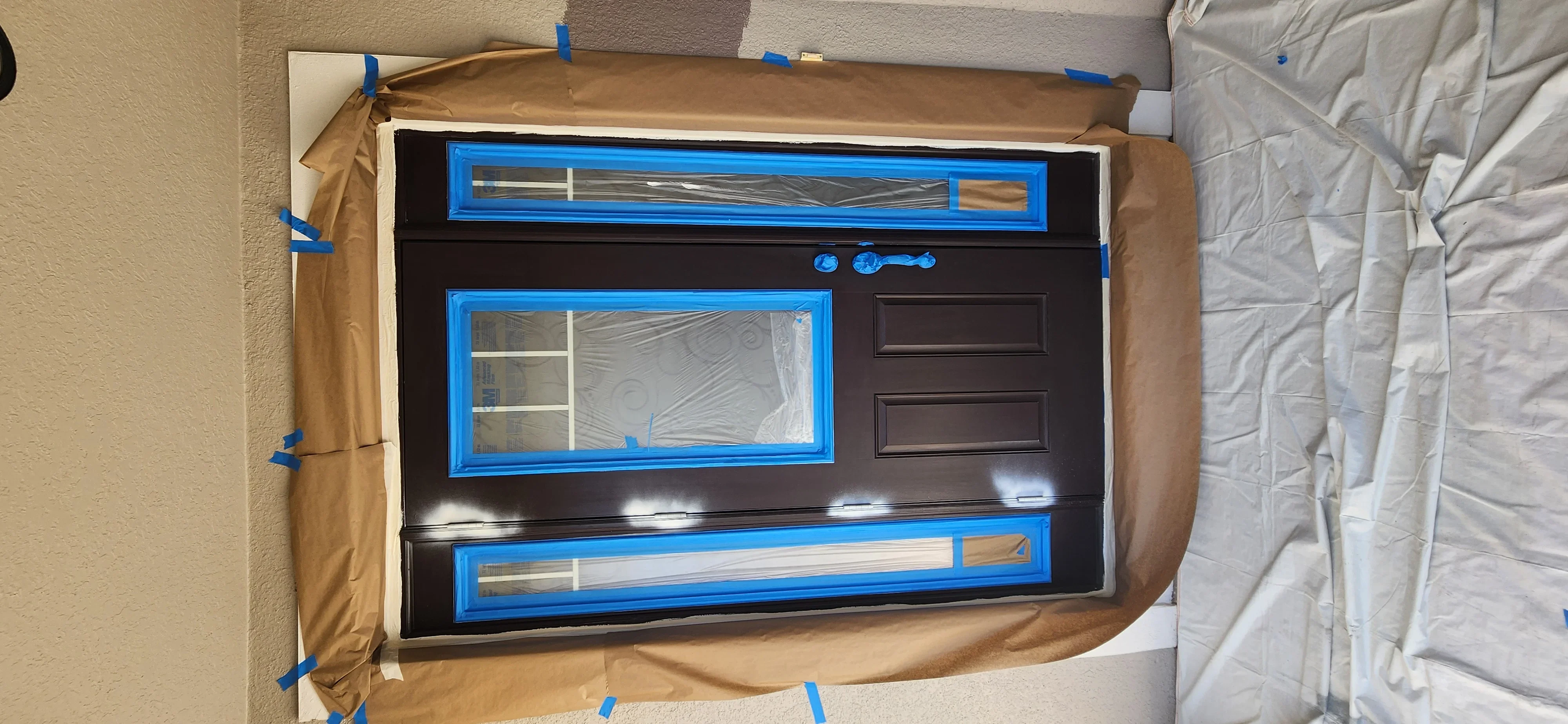 Dark brown garage door with blue trim masking tape, professional paint preparation in progress