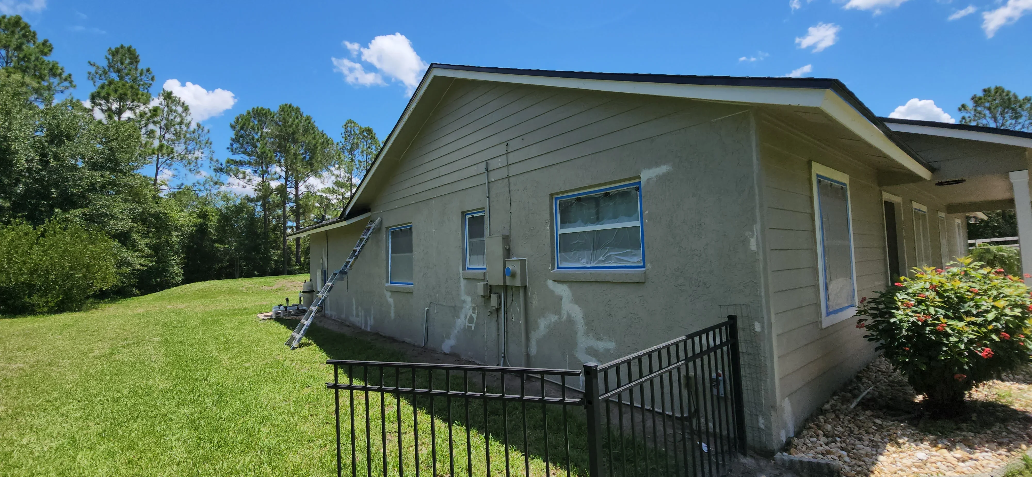 Stucco house exterior with blue-taped windows and ladder setup for painting preparation