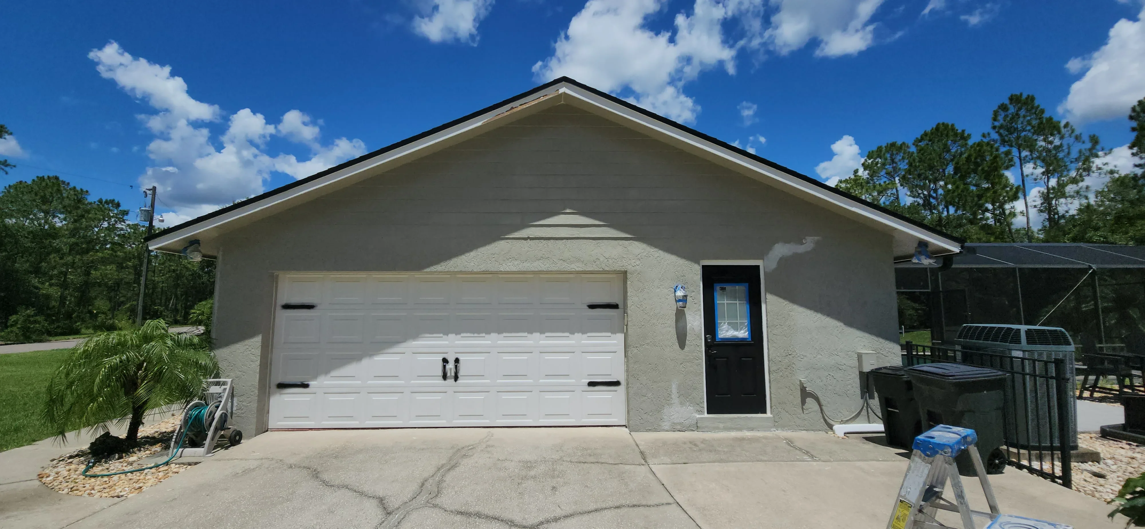Stucco house exterior with white garage door and black entry door, freshly painted