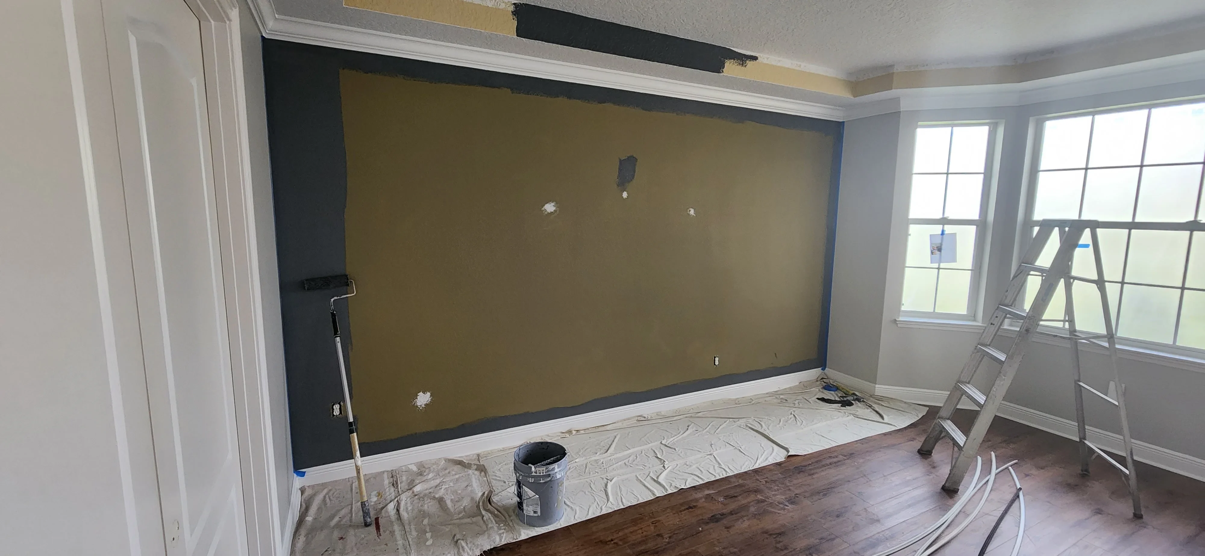 Interior room with gold accent wall, black trim, white crown molding, and protective floor coverings during painting project