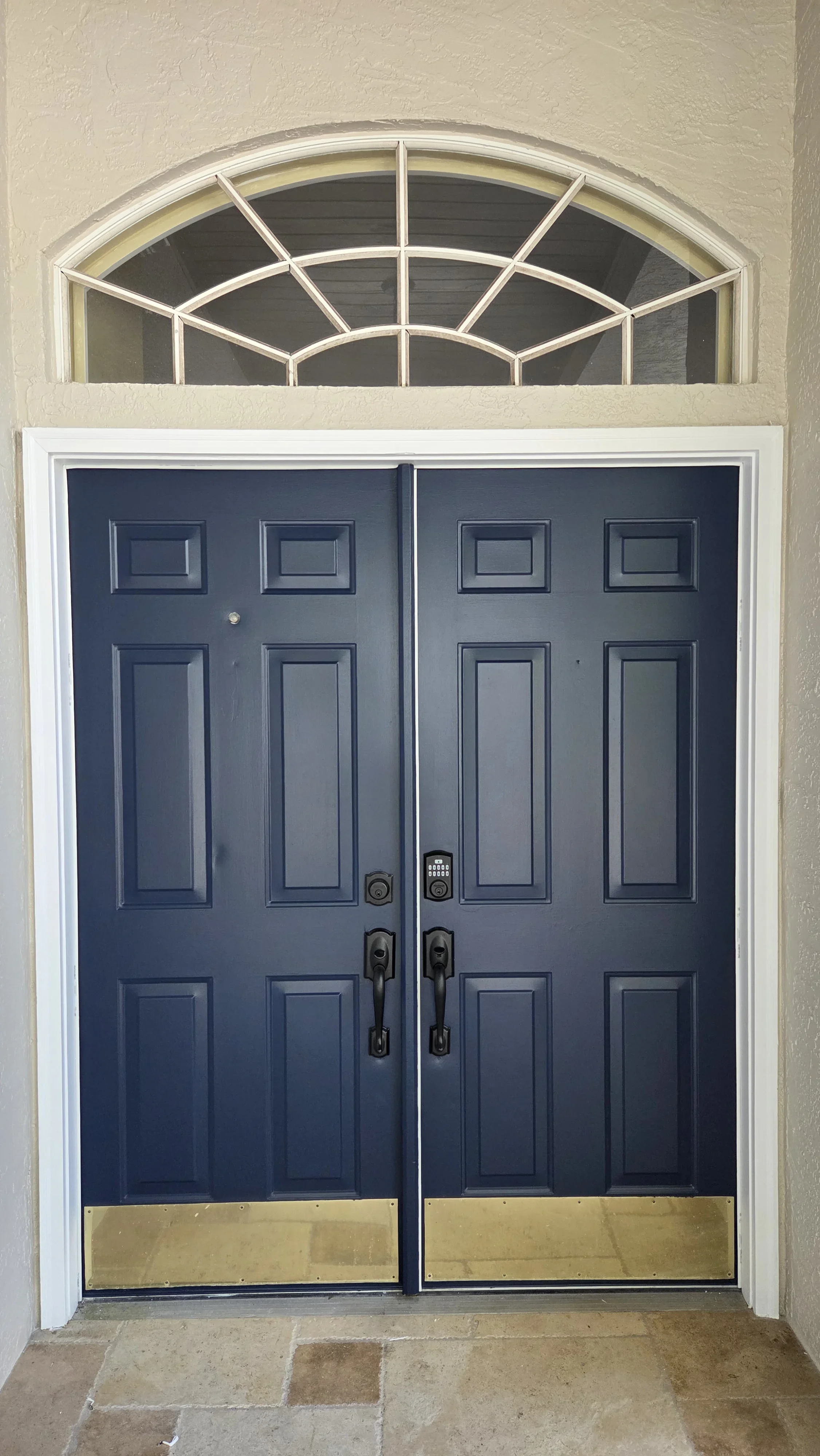 Navy blue double entry doors with six-panel design, bronze hardware, and arched transom window