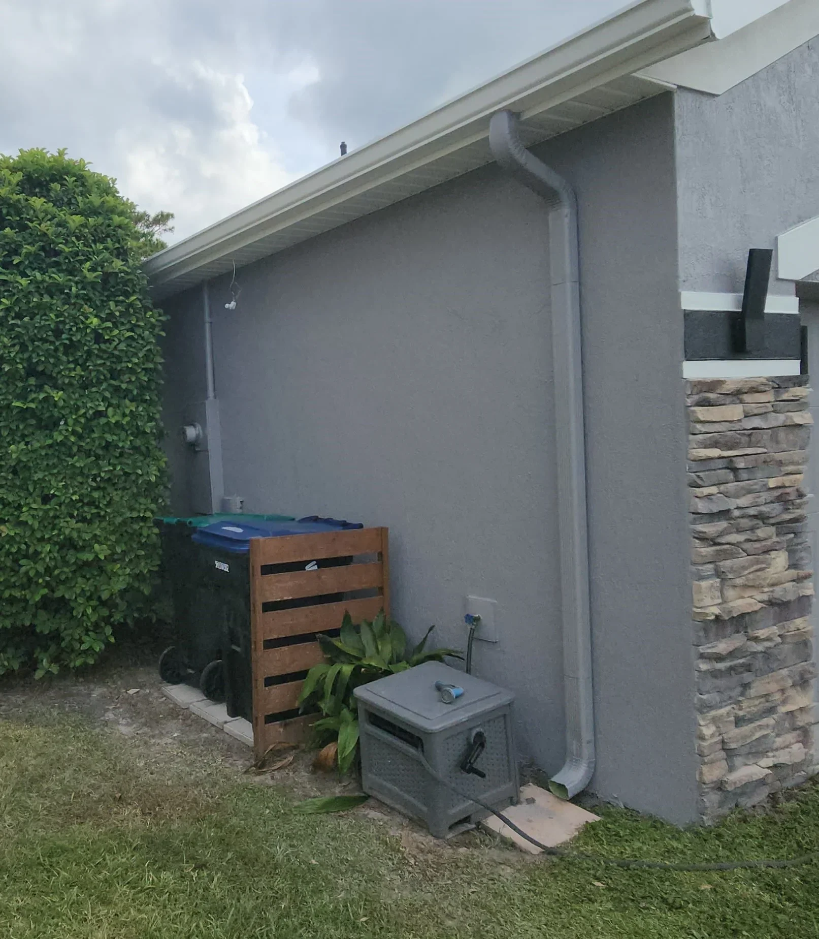 Gray painted exterior wall with trim, stone veneer detail, and downspout installation