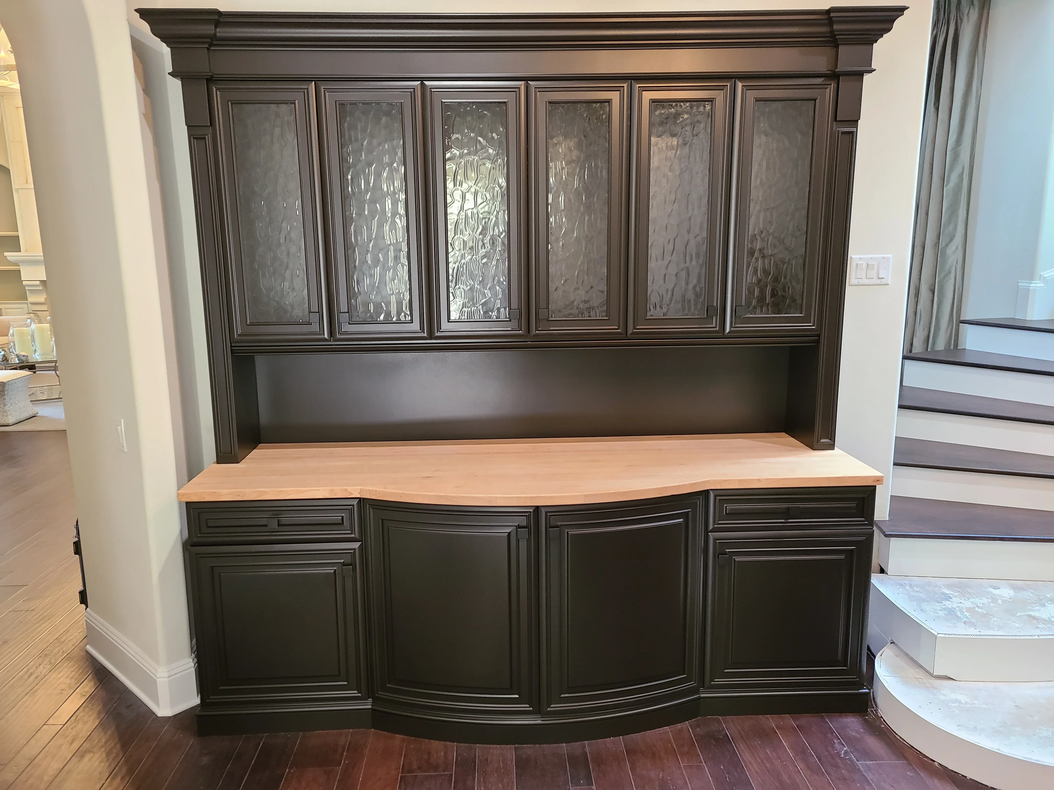 Charcoal-painted built-in cabinetry with glass-front upper cabinets and curved lower storage with natural wood countertop