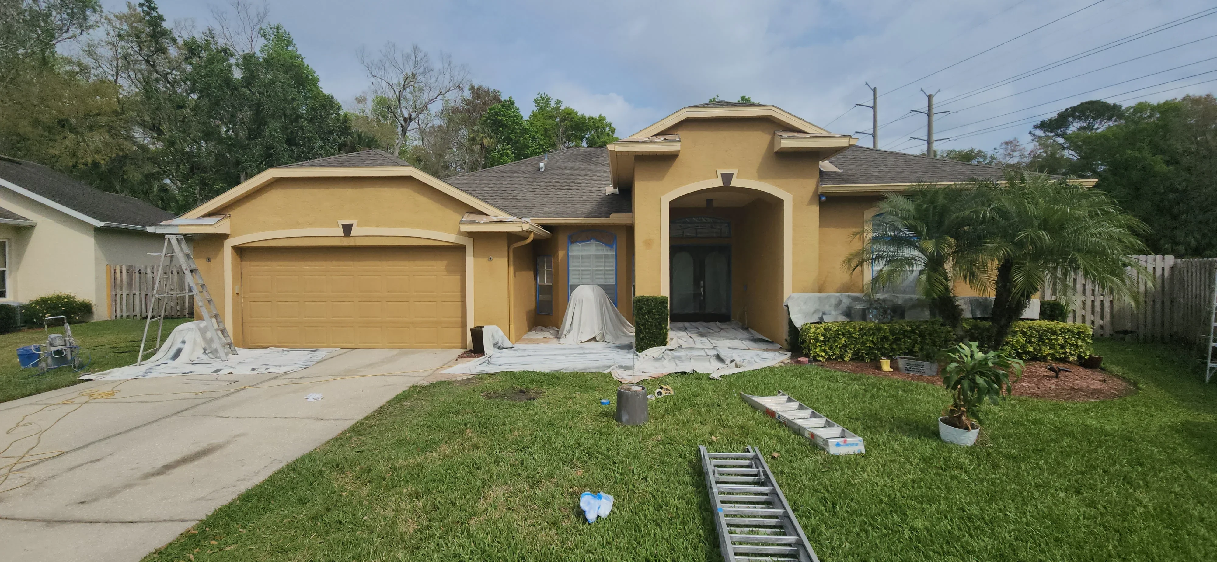 Golden stucco house with protective coverings on entry and landscaping during painting prep