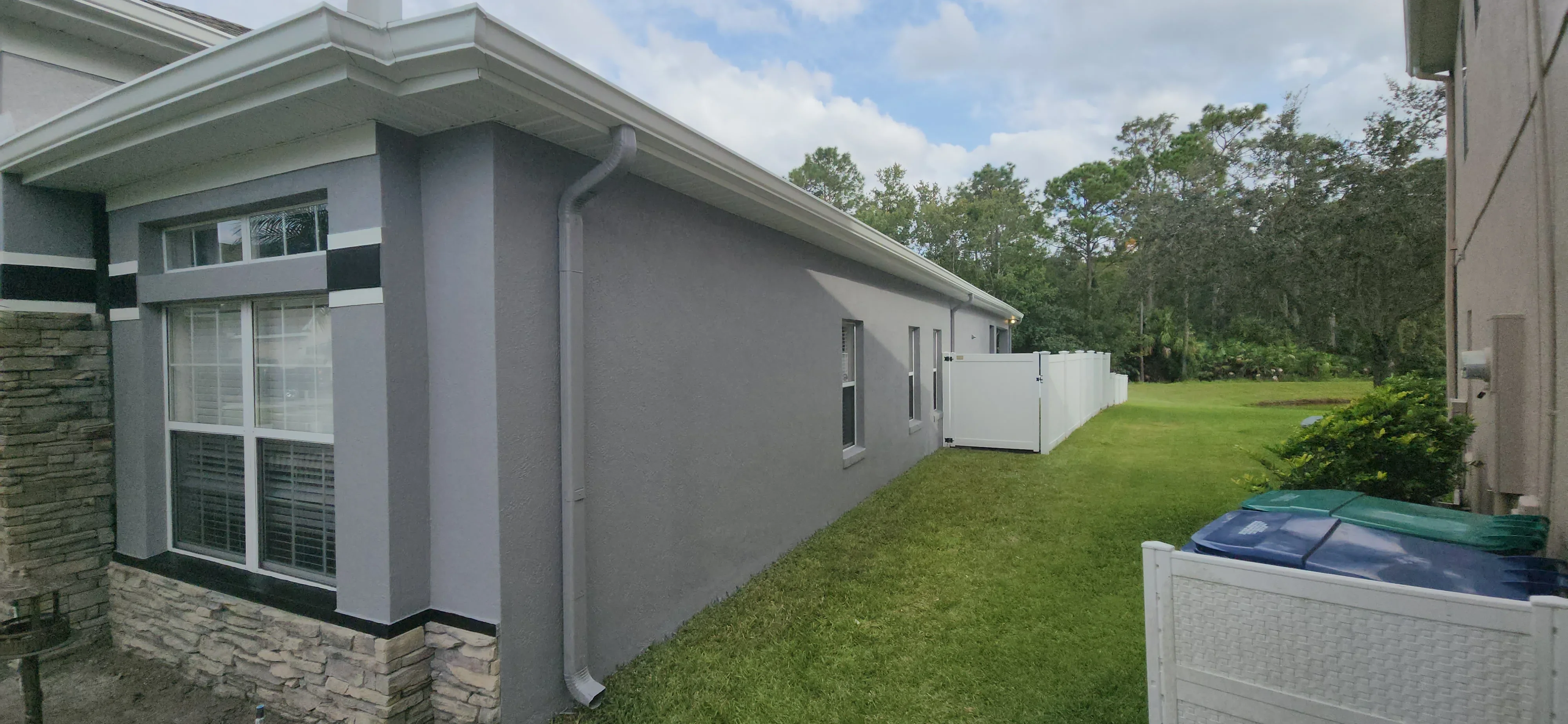 Gray stucco house exterior with white trim, black accent bands, and painted window frames