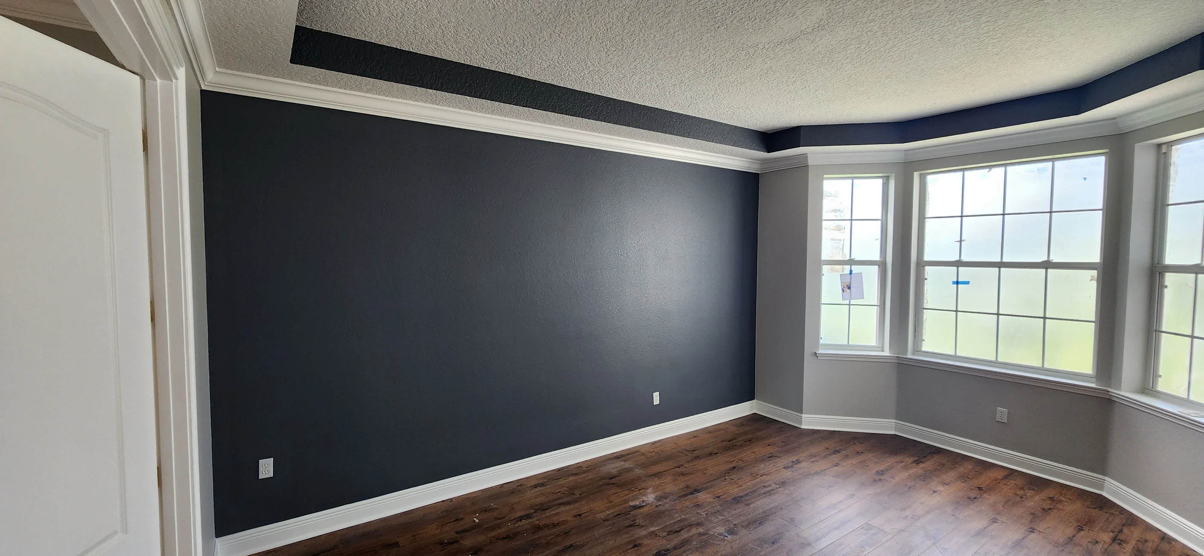 Dark navy accent wall with white trim, textured ceiling, and gray walls in residential interior