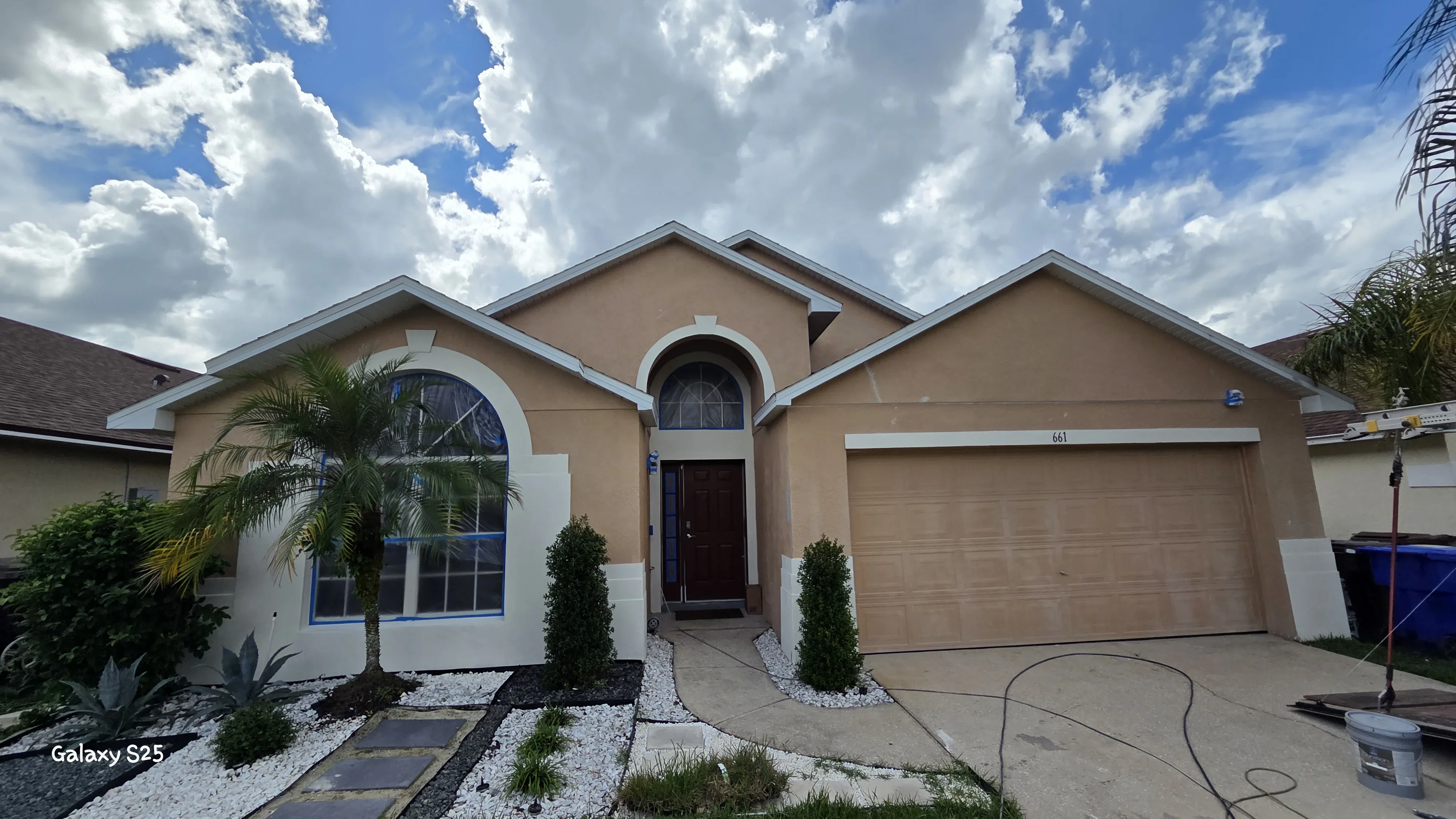 Tan stucco house with white trim, arched windows, and painted garage door