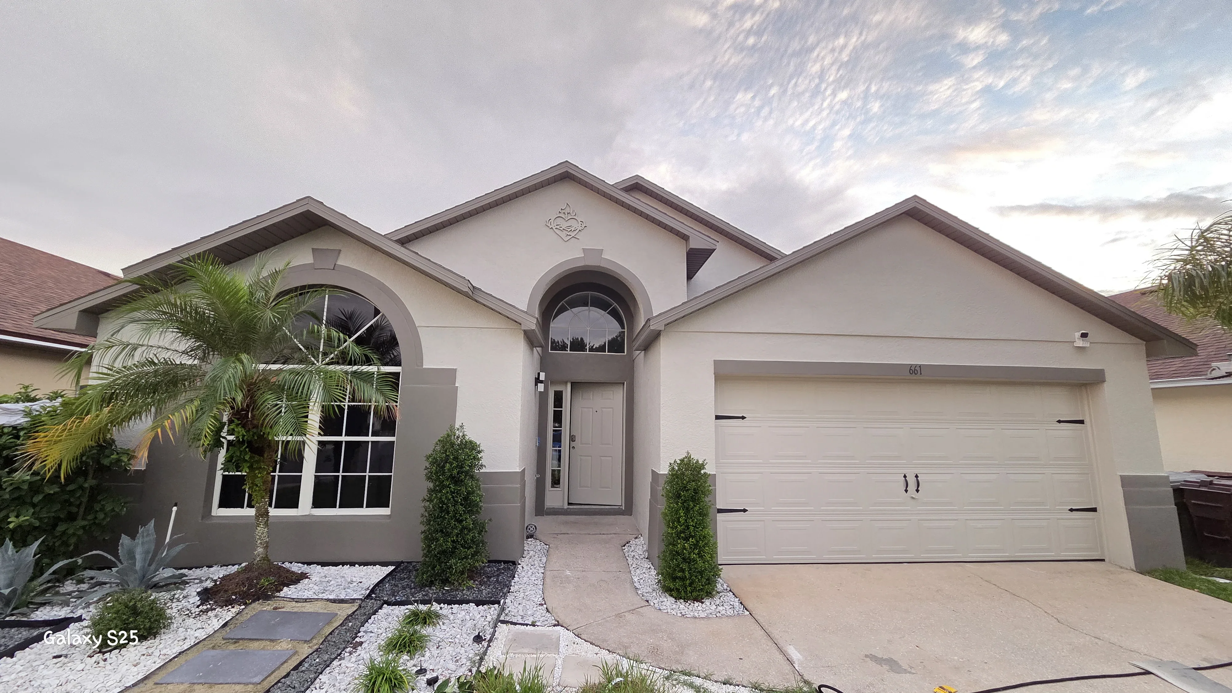 Beige stucco house exterior with painted trim, garage doors, and arched windows