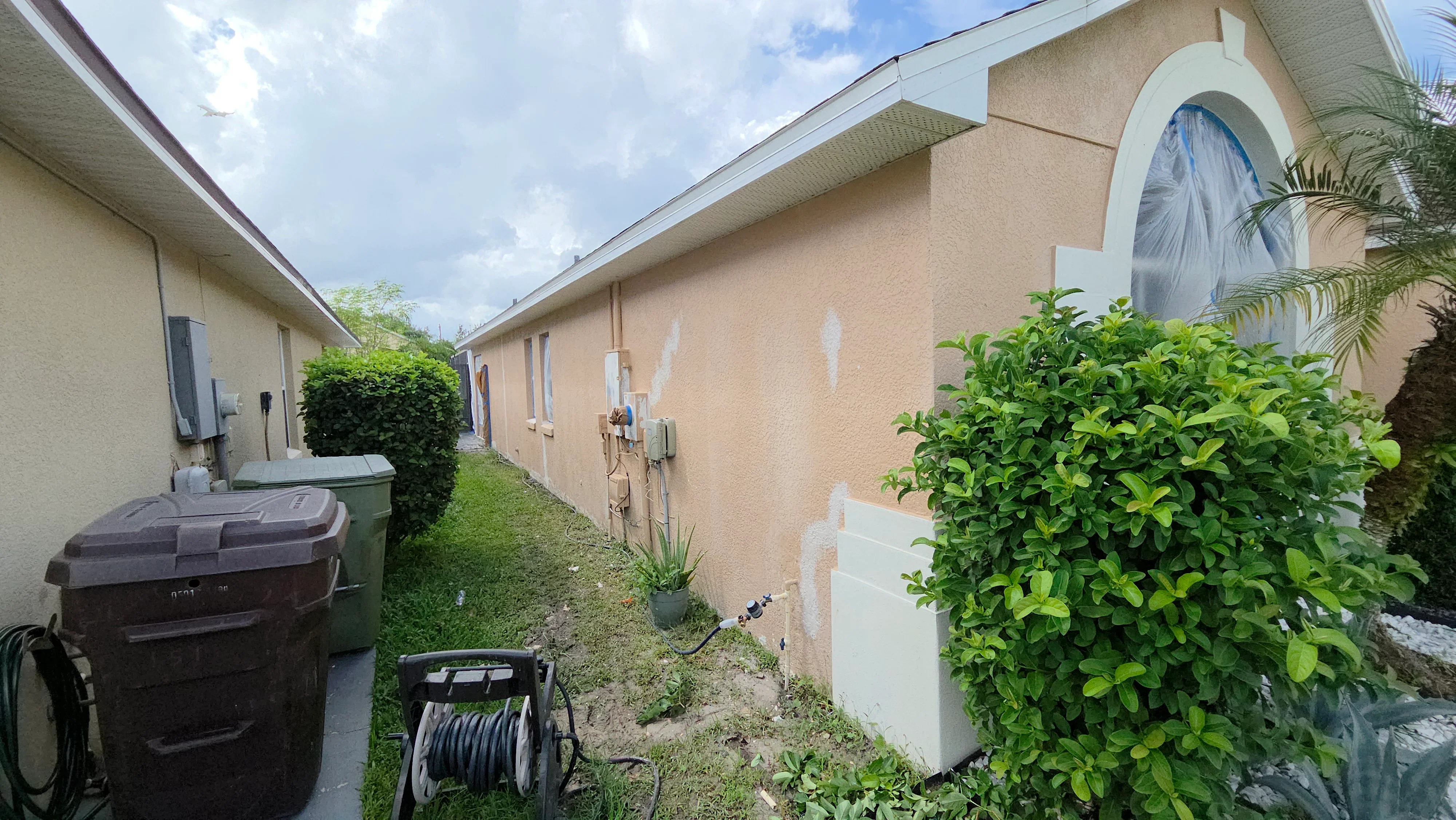 Stucco exterior walls with white protective coverings and masking tape applied before painting