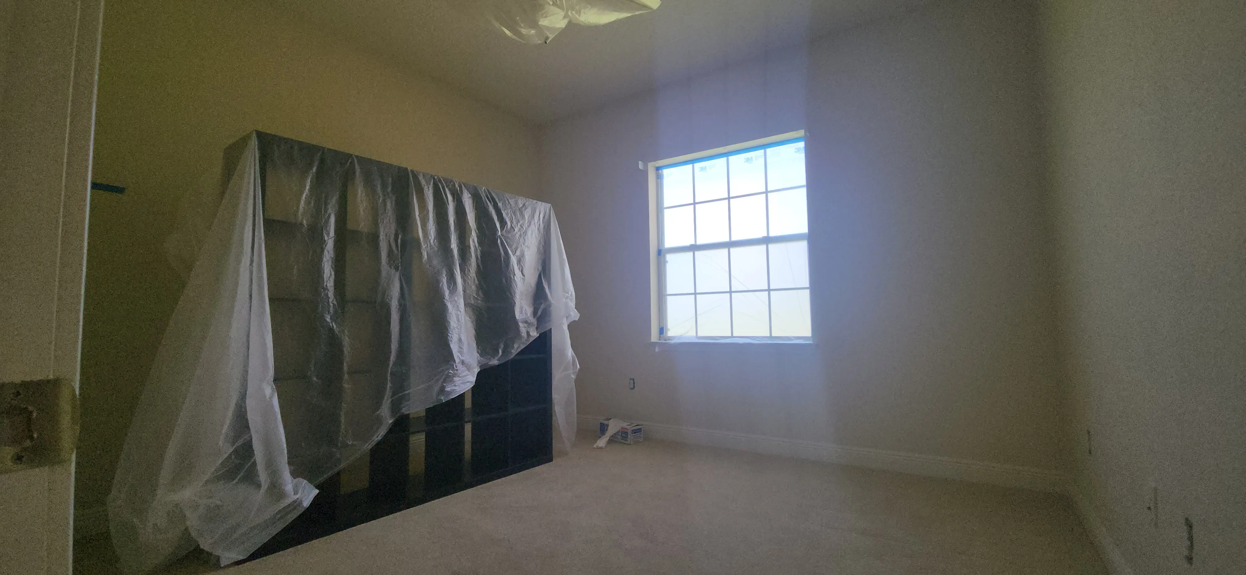 Primed drywall interior with plastic protection covering fixtures and window with grid pattern