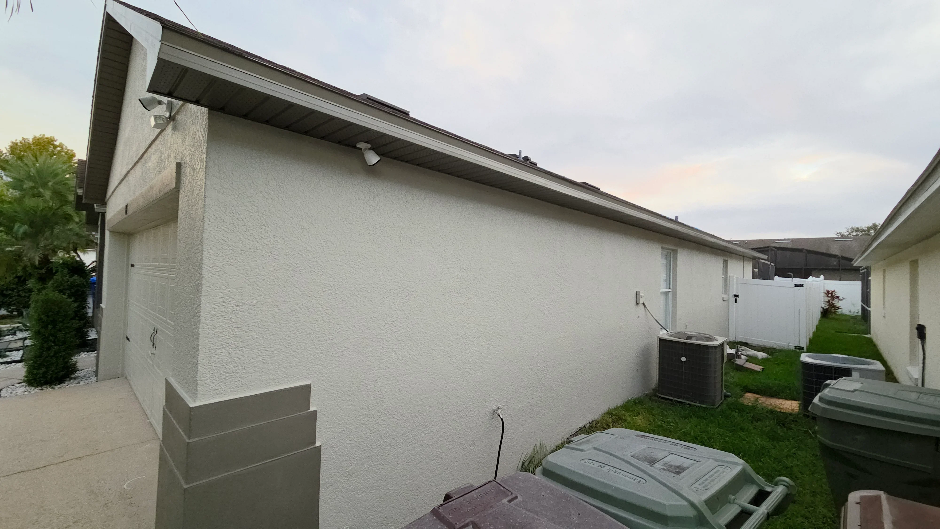 White painted stucco exterior wall with dark roof overhang and concrete foundation