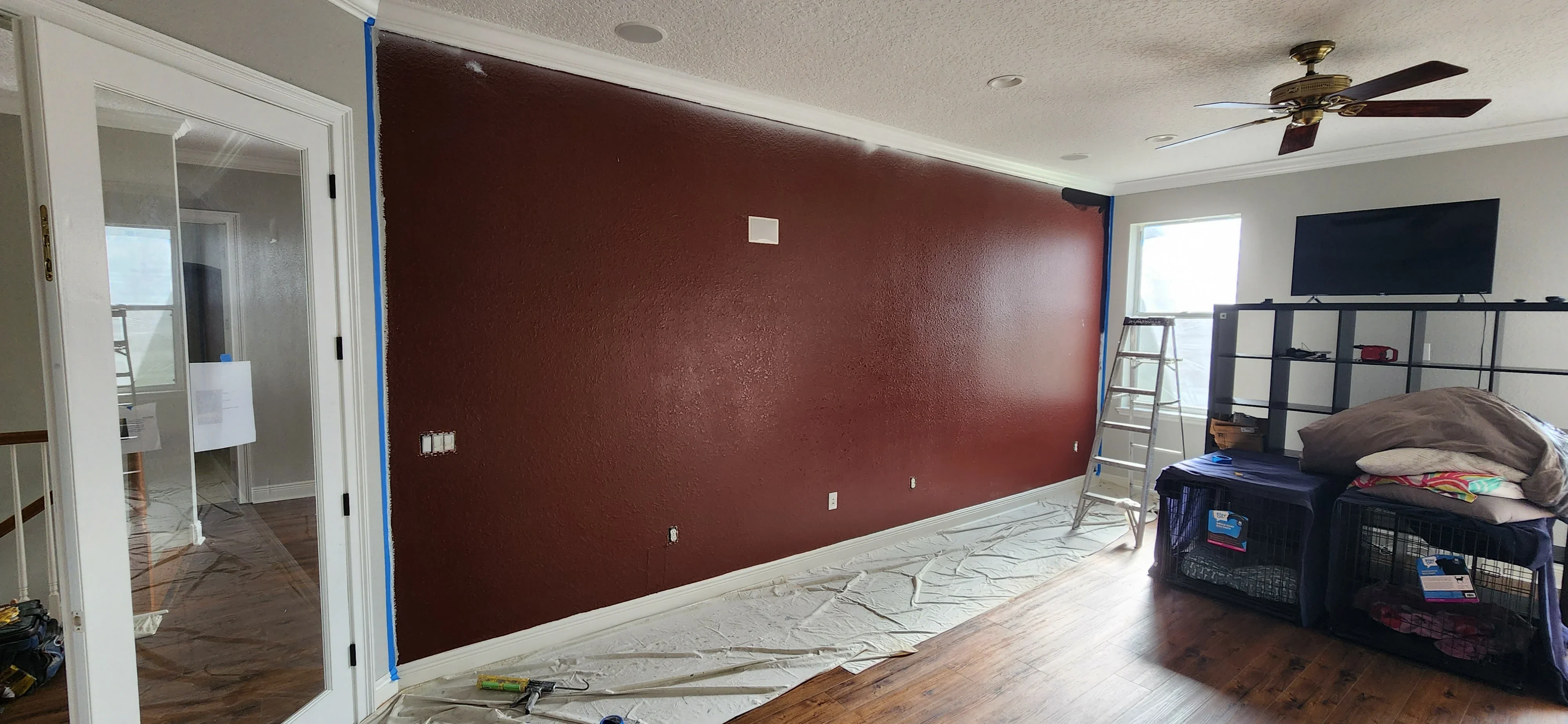 Burgundy accent wall with blue painter's tape masking, electrical outlets, and protective floor covering