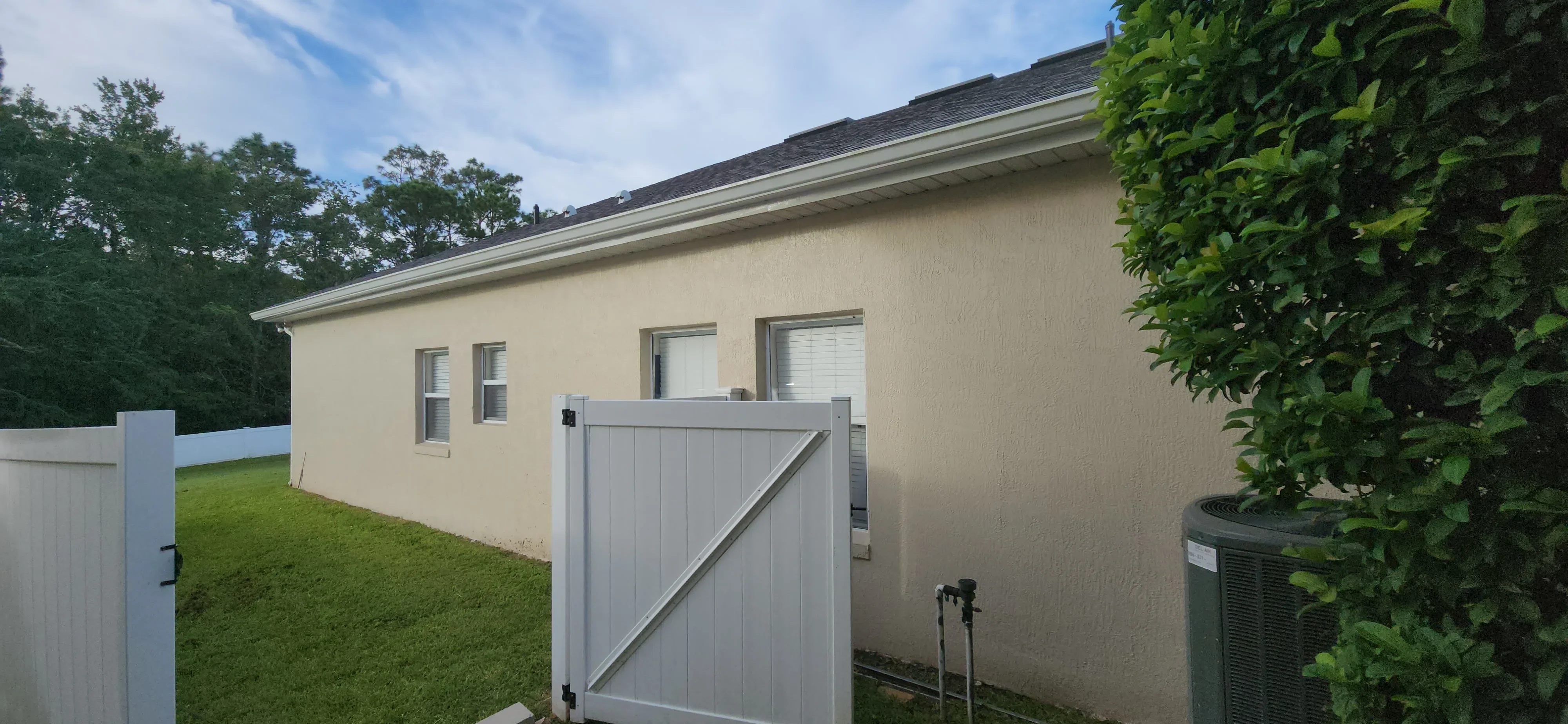 Cream stucco house exterior with white trim, painted windows, and white vinyl gate