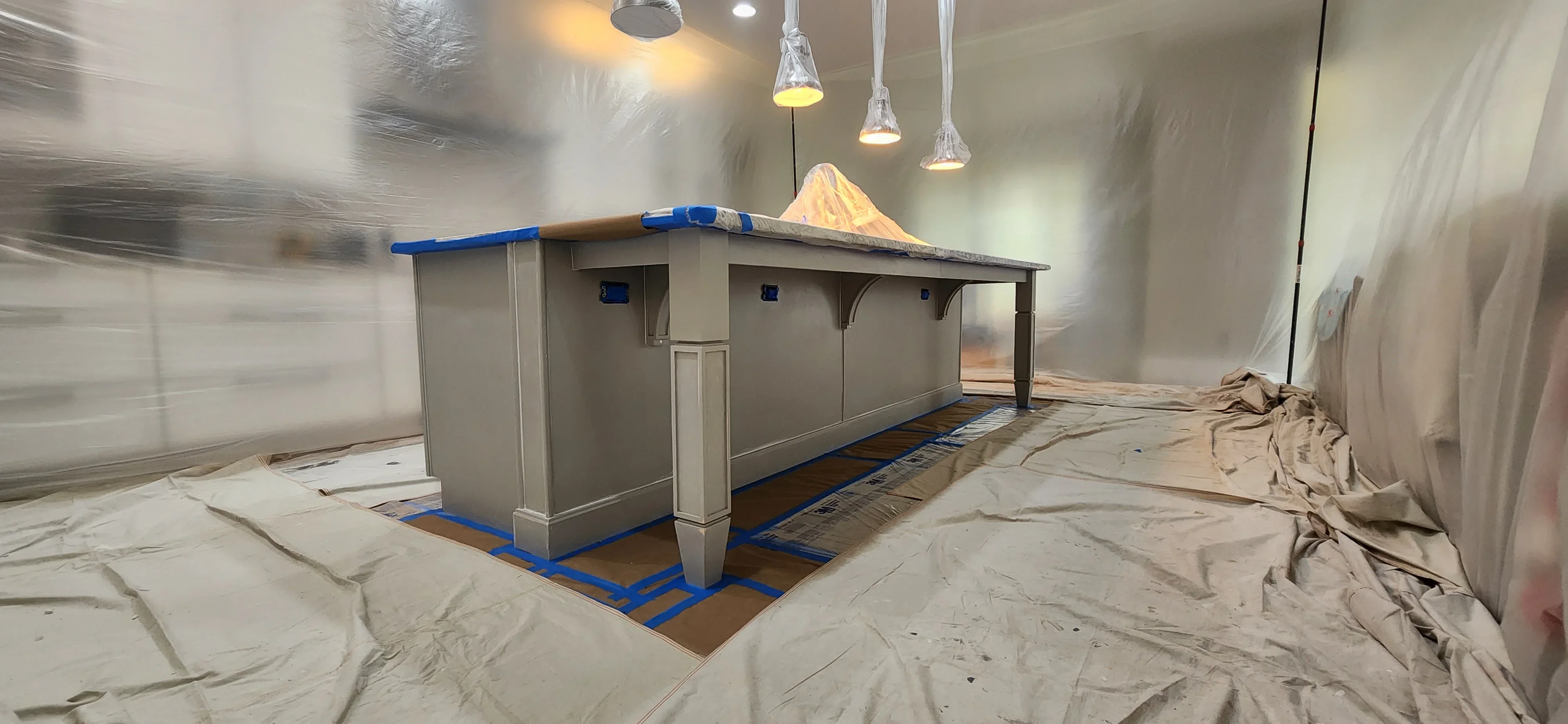 Commercial interior with protected cabinetry, blue tape masking, and drop cloths during painting prep