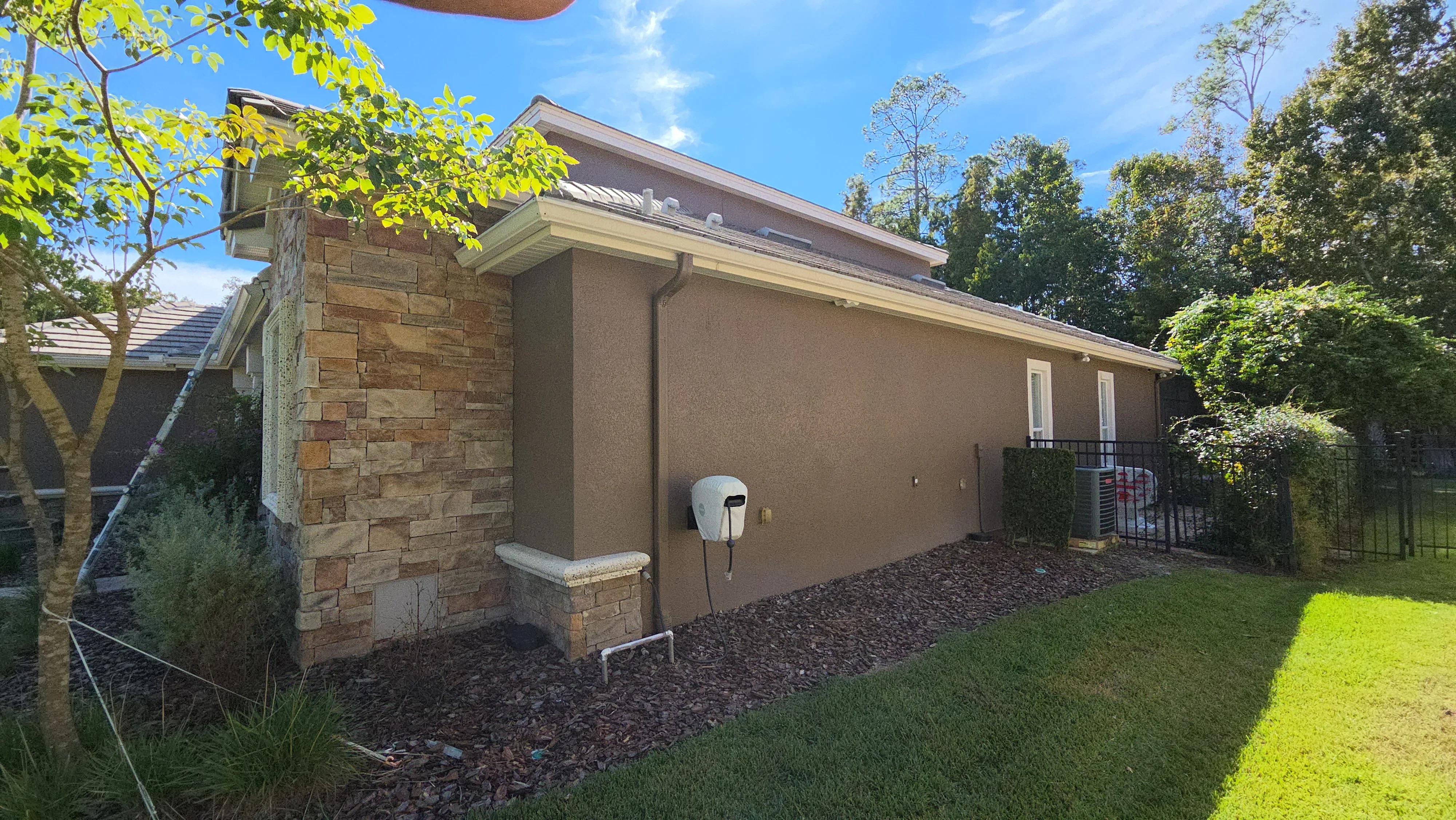 Tan stucco exterior wall with stone veneer chimney and painted trim on residential addition