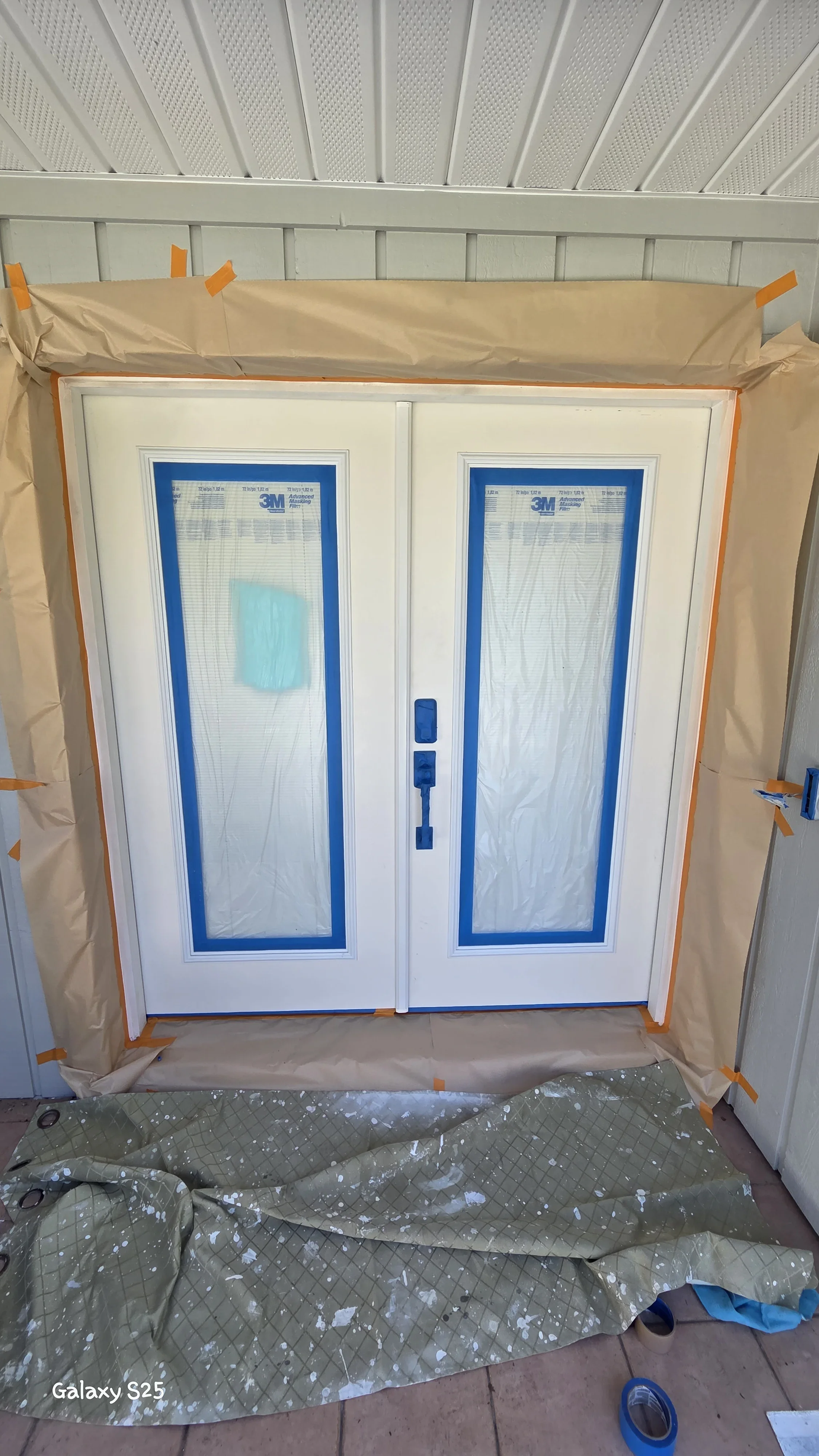 Two white interior doors with blue trim protected by painter's tape and plastic sheeting during installation