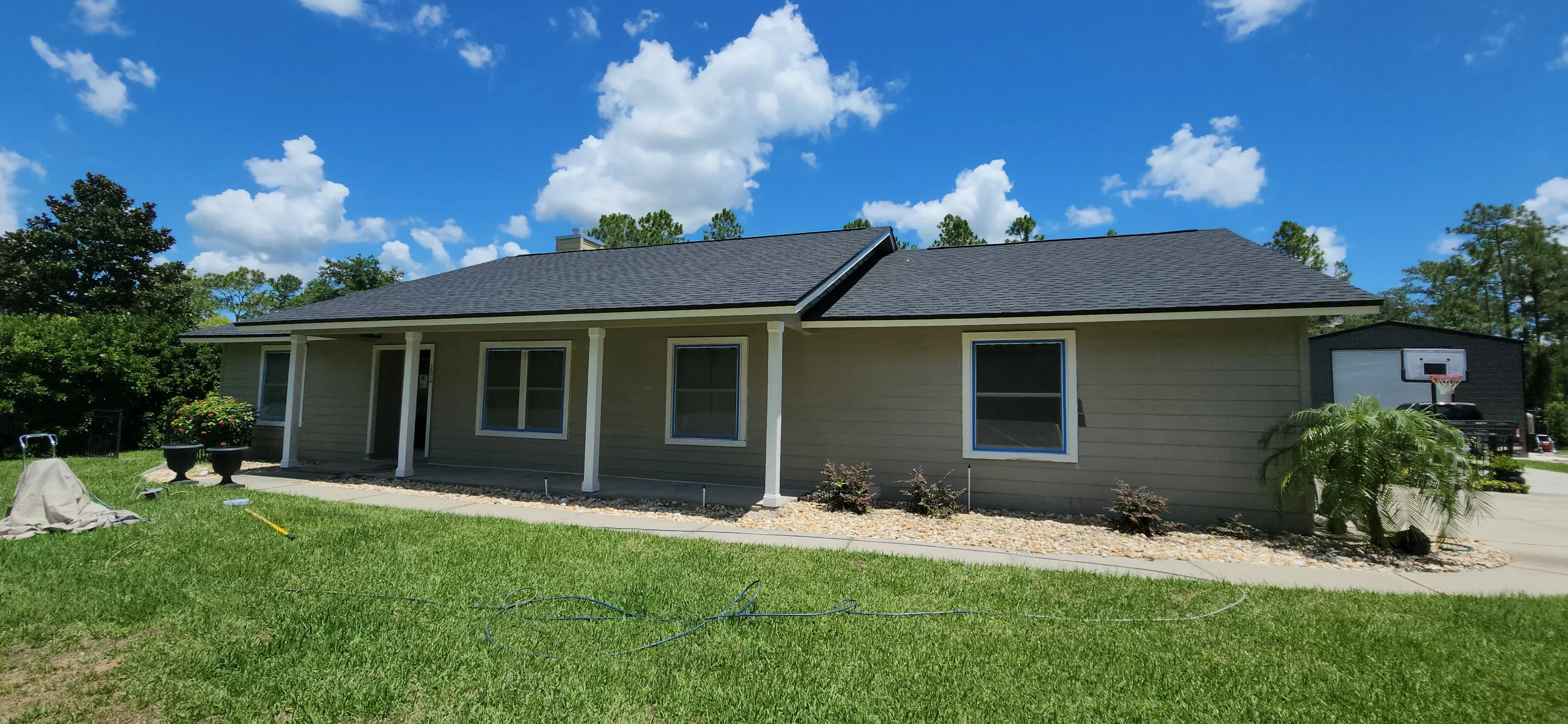 Gray painted house exterior with white trim, blue window frames, and dark asphalt shingle roof