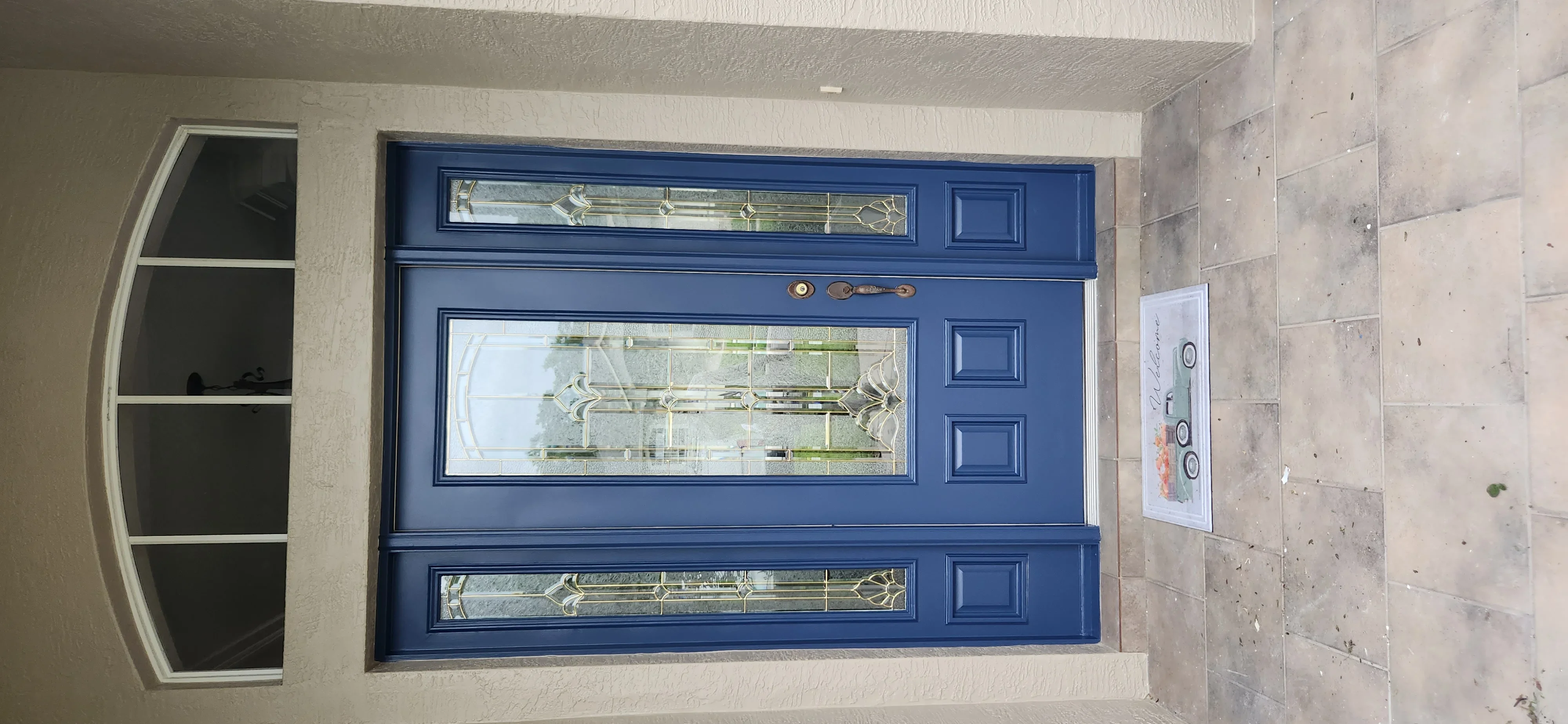 Blue painted entry door with glass panels, decorative sidelights, and brass hardware on stucco exterior
