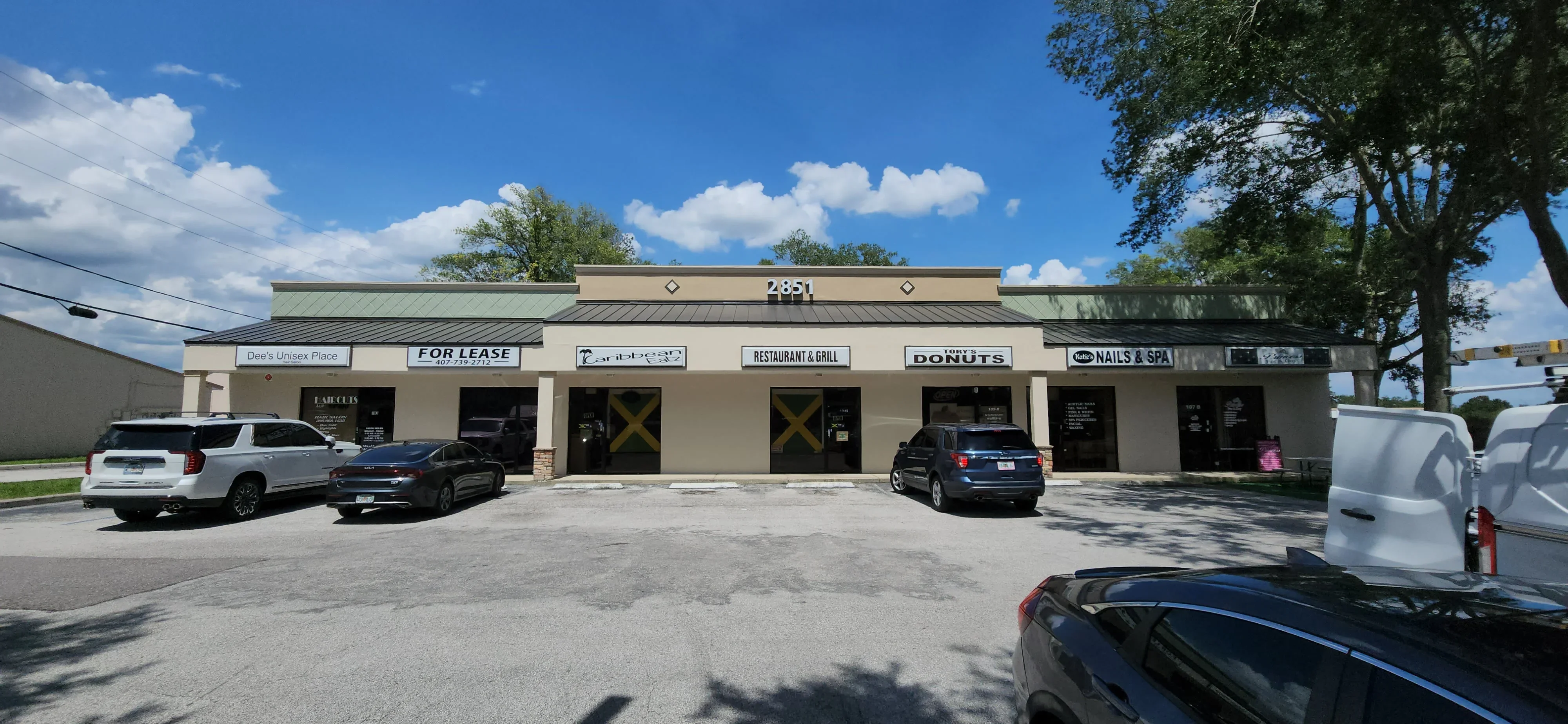 Tan and green painted commercial strip building with metal roof trim and multiple business storefronts